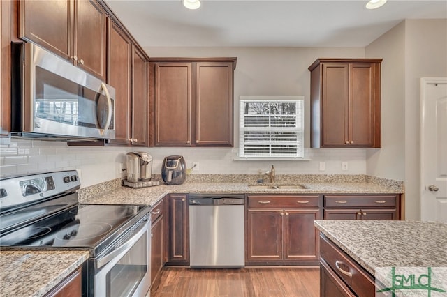 kitchen with sink, backsplash, light hardwood / wood-style floors, stainless steel appliances, and light stone countertops