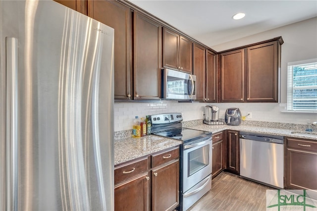 kitchen featuring light wood-type flooring, dark brown cabinetry, stainless steel appliances, and light stone countertops