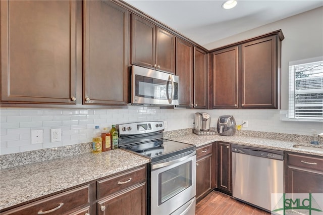 kitchen featuring appliances with stainless steel finishes, light stone counters, dark brown cabinets, light wood-type flooring, and backsplash