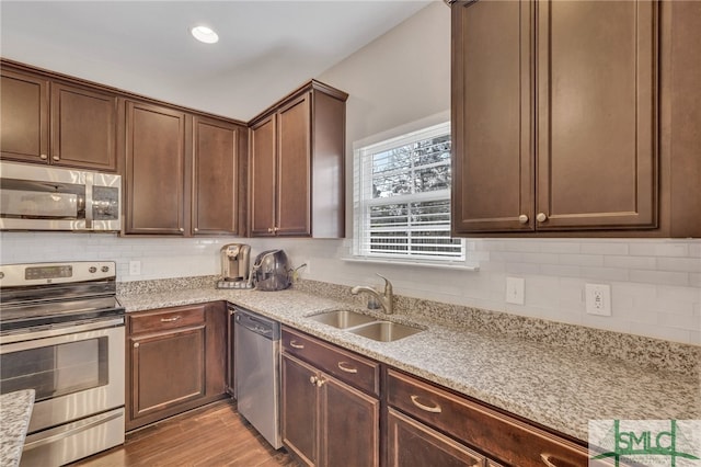 kitchen featuring light stone countertops, appliances with stainless steel finishes, light hardwood / wood-style floors, sink, and dark brown cabinetry