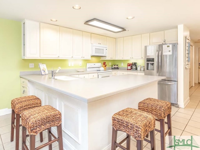 kitchen with white appliances, a breakfast bar, white cabinetry, and light tile flooring