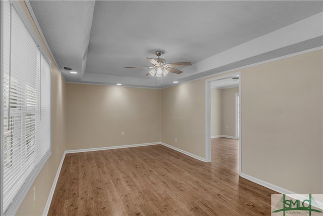 spare room featuring a raised ceiling, light hardwood / wood-style floors, and ceiling fan