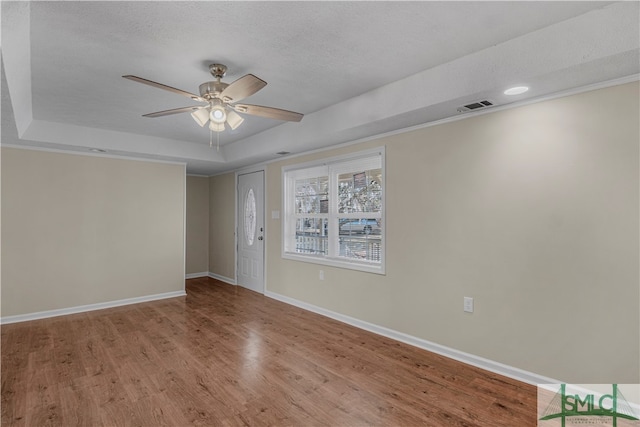 spare room featuring a textured ceiling, a raised ceiling, ceiling fan, and light wood-type flooring