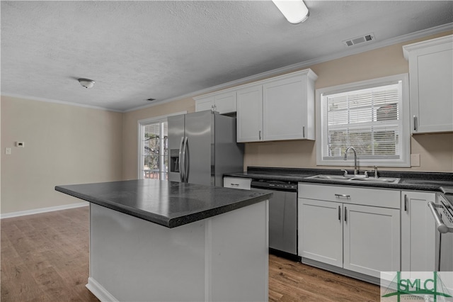 kitchen with appliances with stainless steel finishes, a center island, light hardwood / wood-style floors, sink, and white cabinetry