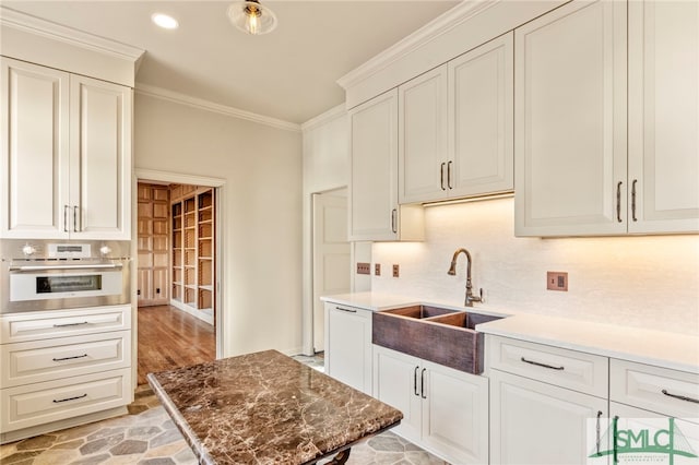 kitchen with stone counters, crown molding, light hardwood / wood-style flooring, stainless steel oven, and sink