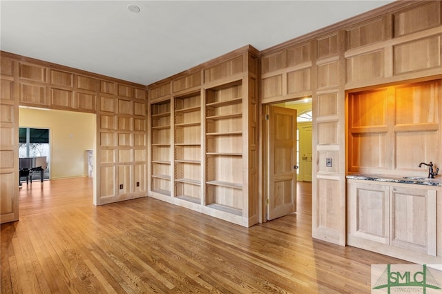 spare room with light wood-type flooring, wooden walls, built in features, and sink