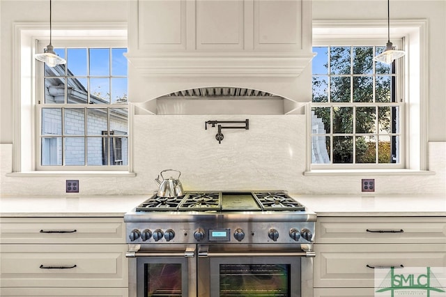 kitchen featuring tasteful backsplash, high end stove, decorative light fixtures, and custom range hood