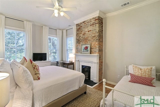 bedroom featuring multiple windows, crown molding, ceiling fan, and a brick fireplace