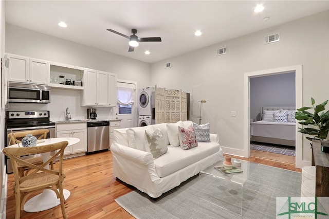 living room with stacked washing maching and dryer, ceiling fan, sink, and light wood-type flooring