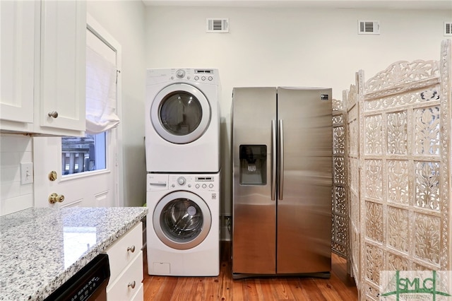 clothes washing area with stacked washer and clothes dryer and light wood-type flooring