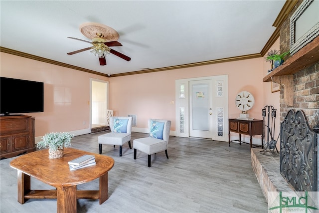 living room with a brick fireplace, ornamental molding, ceiling fan, and light wood-type flooring