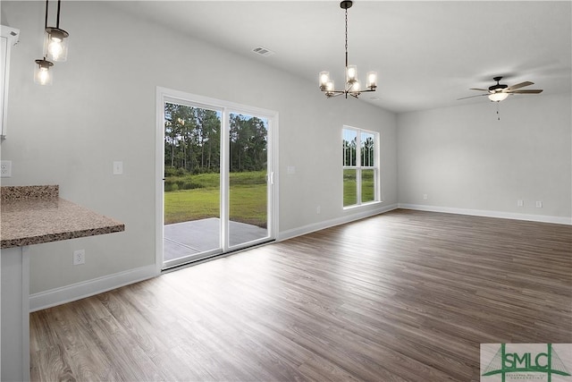 unfurnished dining area featuring ceiling fan with notable chandelier, visible vents, baseboards, and wood finished floors