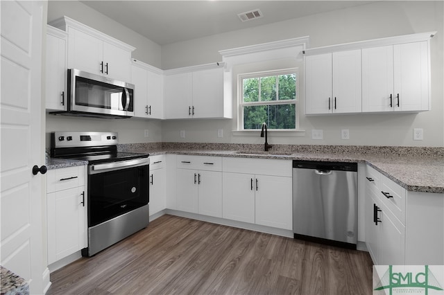 kitchen featuring white cabinets, light hardwood / wood-style floors, light stone countertops, sink, and stainless steel appliances