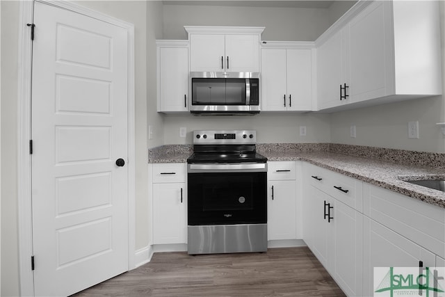 kitchen featuring stainless steel appliances, white cabinetry, light stone counters, and light hardwood / wood-style flooring