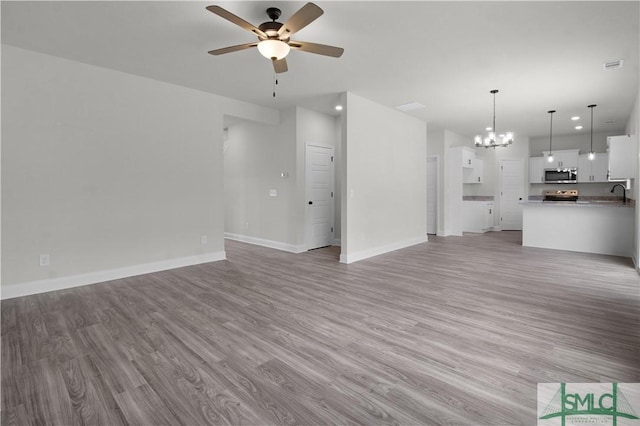 unfurnished living room with light wood-type flooring, visible vents, baseboards, and ceiling fan with notable chandelier