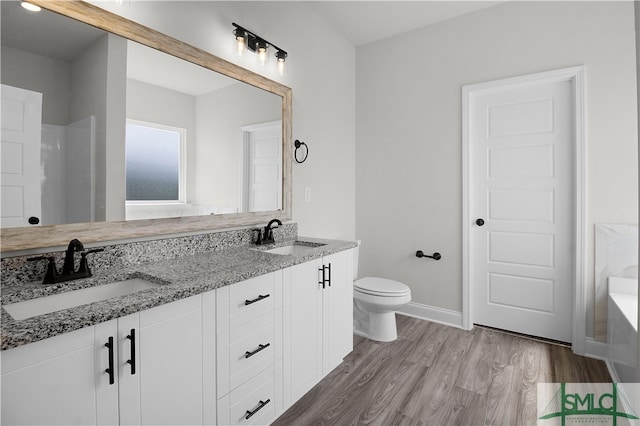 bathroom featuring hardwood / wood-style flooring, a bathtub, dual vanity, and toilet