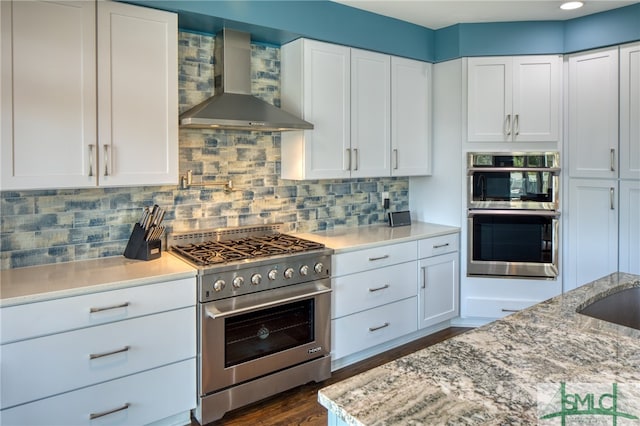 kitchen featuring appliances with stainless steel finishes, white cabinetry, and wall chimney exhaust hood