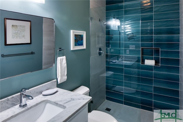 bathroom with toilet, a tile shower, and vanity