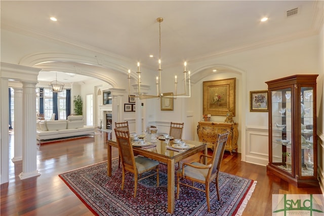 dining area with crown molding, dark wood-type flooring, a notable chandelier, and decorative columns