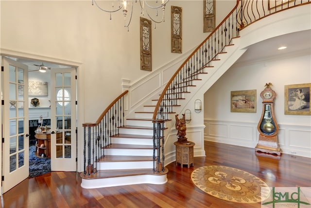 stairs with dark hardwood / wood-style flooring, french doors, ceiling fan with notable chandelier, and crown molding