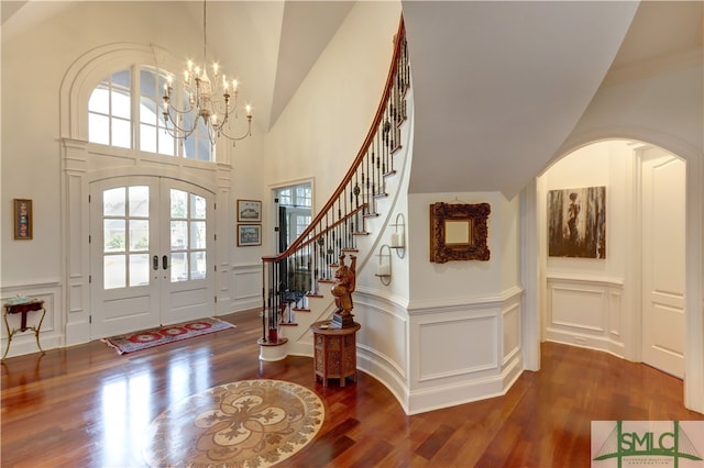 foyer entrance with high vaulted ceiling, dark wood-type flooring, french doors, and an inviting chandelier