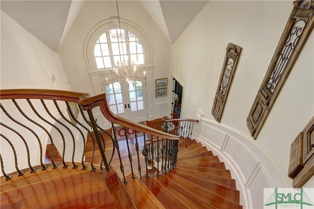 staircase with hardwood / wood-style floors, high vaulted ceiling, french doors, and a chandelier