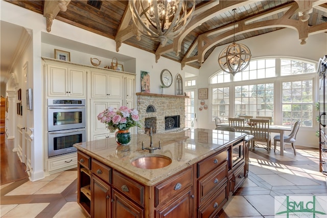 kitchen featuring a stone fireplace, stainless steel appliances, a center island with sink, a notable chandelier, and light tile floors