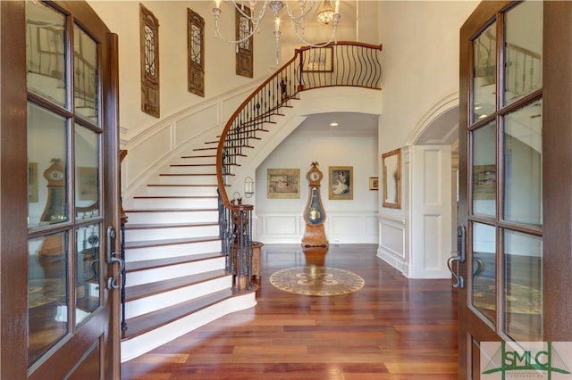 entryway with french doors, a towering ceiling, dark hardwood / wood-style floors, an inviting chandelier, and ornamental molding