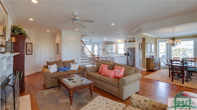 living room with crown molding, ceiling fan with notable chandelier, a healthy amount of sunlight, and light hardwood / wood-style flooring