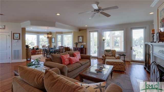 living room featuring a tile fireplace, hardwood / wood-style floors, ornamental molding, a wealth of natural light, and ceiling fan with notable chandelier