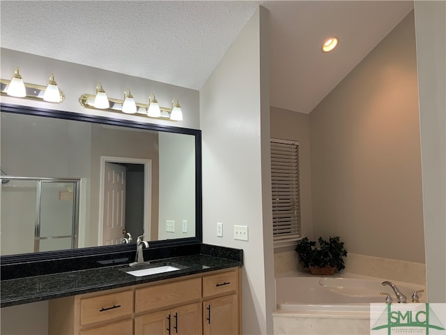 bathroom with a relaxing tiled bath, vanity, a textured ceiling, and lofted ceiling