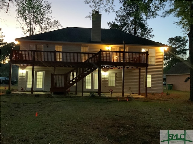 back house at dusk with a deck and a lawn