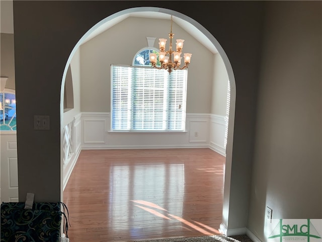 empty room featuring vaulted ceiling, light wood-type flooring, and a chandelier