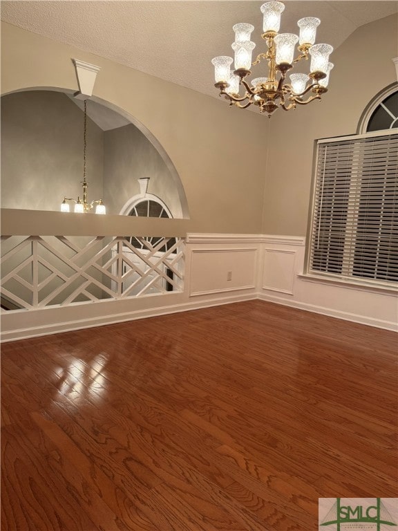 unfurnished room with lofted ceiling, an inviting chandelier, and dark hardwood / wood-style floors