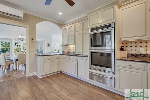 kitchen with stainless steel double oven, a wall unit AC, backsplash, and ceiling fan with notable chandelier