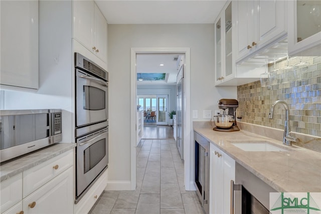 kitchen featuring light stone counters, stainless steel appliances, backsplash, sink, and white cabinetry