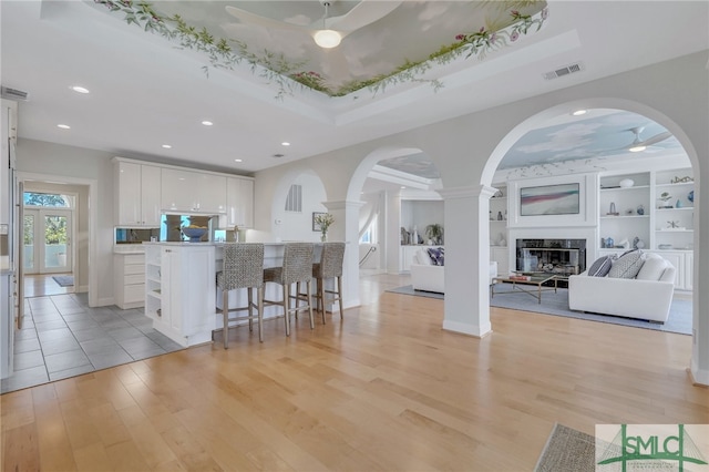 kitchen with a breakfast bar, decorative columns, a raised ceiling, light tile floors, and white cabinets