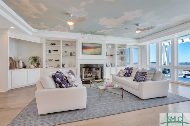 living room with a high end fireplace, ceiling fan, a wealth of natural light, and light wood-type flooring