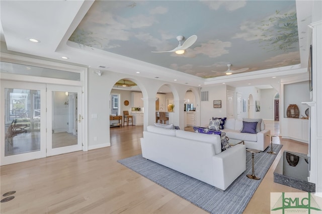 living room featuring ceiling fan, light hardwood / wood-style flooring, and a tray ceiling