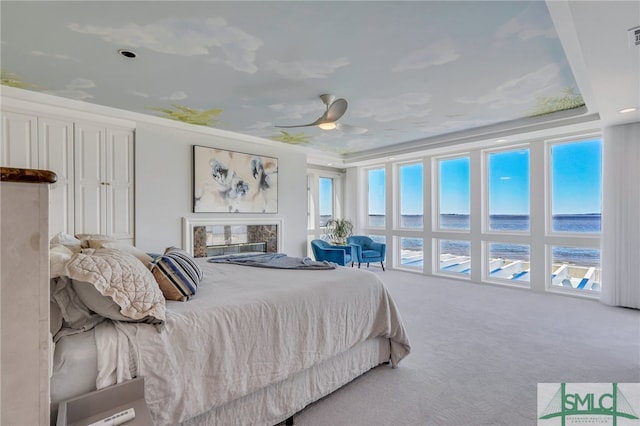 carpeted bedroom with a water view, ceiling fan, and a premium fireplace