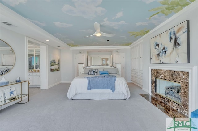 bedroom featuring a fireplace, connected bathroom, light carpet, and ceiling fan