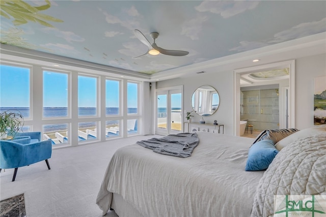 carpeted bedroom featuring ceiling fan, a water view, a tray ceiling, and connected bathroom