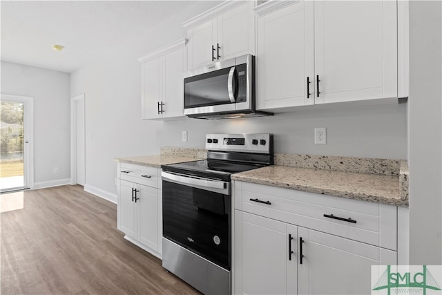 kitchen featuring appliances with stainless steel finishes, white cabinetry, light stone countertops, and light wood-type flooring