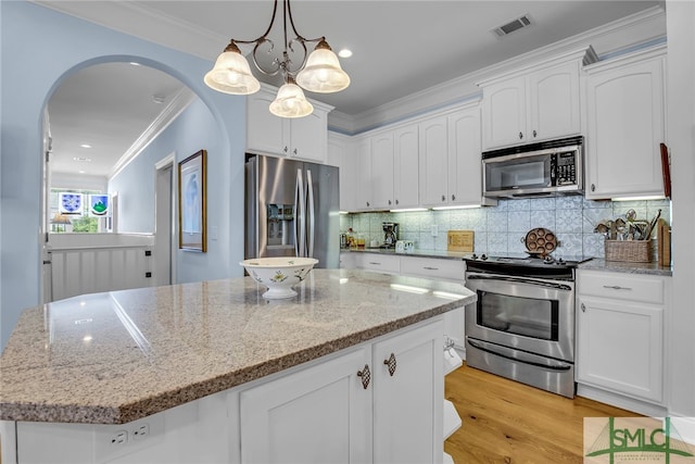 kitchen featuring white cabinets, backsplash, appliances with stainless steel finishes, a kitchen island, and light wood-type flooring