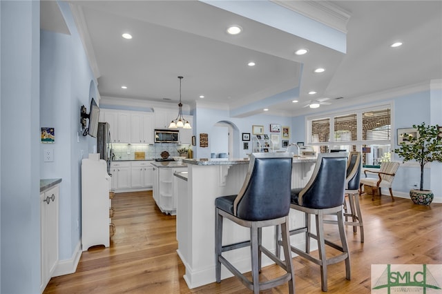 kitchen with pendant lighting, an island with sink, a breakfast bar area, light hardwood / wood-style floors, and white cabinetry