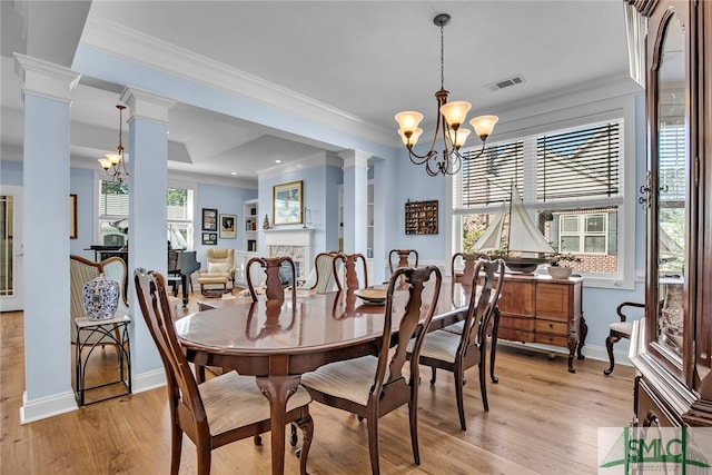 dining room featuring a notable chandelier, ornamental molding, light wood-type flooring, and decorative columns