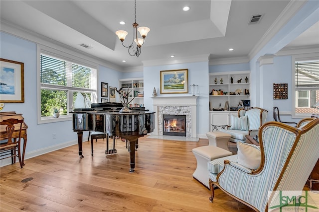 living area with crown molding, a notable chandelier, a fireplace, light hardwood / wood-style flooring, and a tray ceiling