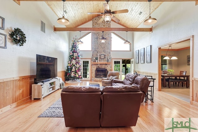 living room featuring a stone fireplace, ceiling fan, light hardwood / wood-style floors, high vaulted ceiling, and beam ceiling