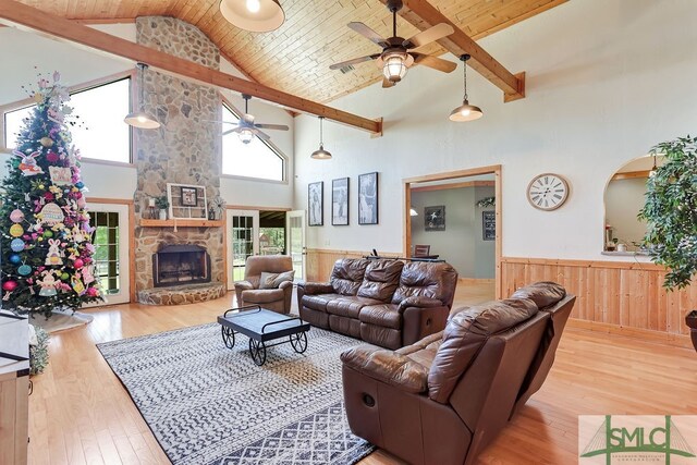 living room featuring high vaulted ceiling, ceiling fan, light wood-type flooring, and a stone fireplace