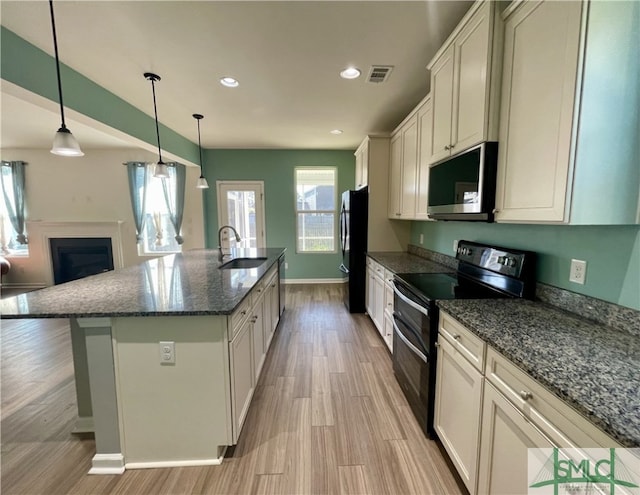 kitchen featuring black appliances, sink, light wood-type flooring, an island with sink, and decorative light fixtures